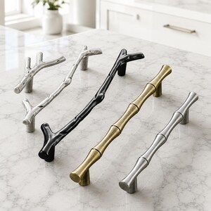 May include: Four cabinet pulls arranged in a row. Two pulls feature a textured, branch-like design in silver and black finishes. Two pulls feature a smooth, segmented bamboo-inspired design in brushed gold and polished silver metallic finishes.
