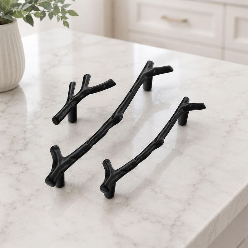 May include: Three matte black cabinet pulls shaped like tree branches. Each handle features a textured, organic form with small offshoot twigs, mounted on two cylindrical posts. The set includes one shorter pull and two longer, slender pulls.