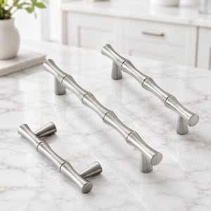 May include: Three silver-toned metal cabinet pulls with a segmented bamboo-inspired design. Each handle features a smooth, polished finish and two conical mounting posts that elevate the bar from the surface, creating a uniform look.
