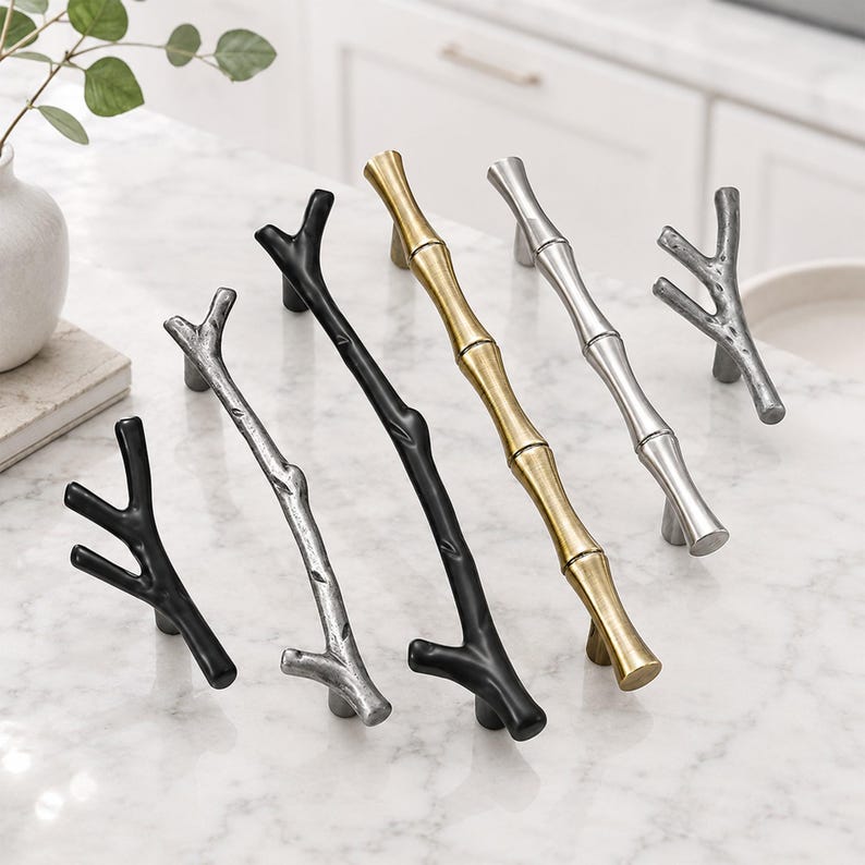 May include: A collection of five cabinet pulls in various finishes and shapes. Two pulls are matte black with a branch-like design, two are silver with a textured branch or bamboo-like appearance, and one is a gold-toned bamboo-style handle.