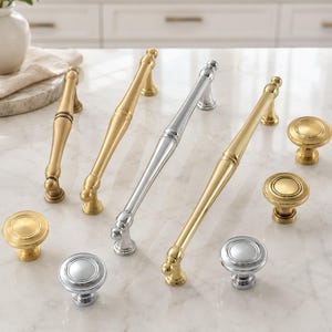 May include: A collection of cabinet hardware including four elongated metal pulls and four round knobs. The hardware features a mix of polished gold and polished silver finishes, each with a smooth, tapered design and rounded mounting bases.