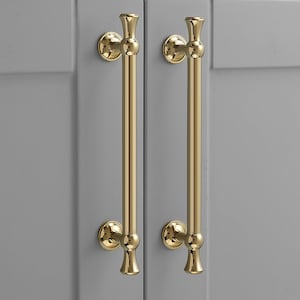 K&ouml;nnte beinhalten: Zwei vertikale Schrankgriffe mit poliertem Gold-Finish. Jeder Griff besteht aus einer langen, glatten zylindrischen Stange mit dekorativen abgerundeten Endst&uuml;cken oben und unten, befestigt durch zwei kreisf&ouml;rmige Montageplatten.