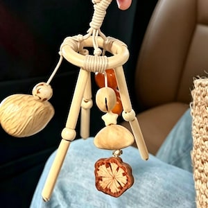 May include: A hanging mobile featuring a central light-coloured wooden ring with three legs. Suspended from the ring are various natural elements including a textured walnut, a small wooden star, a smooth wooden bead, and a carved flower-shaped piece.