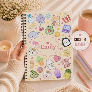 May include: A spiral-bound notebook with a cream-coloured cover featuring various colourful kawaii-style illustrations of food, animals, and objects. The centre displays the name Emily inside a scalloped pink frame, with a circular sticker reading CUSTOM NAME!