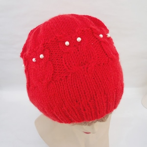 May include: Red knitted beanie with a cable knit pattern and white pearl embellishments.