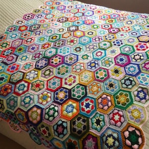 May include: A colourful crocheted blanket made of hexagonal shapes in various colours, including pink, blue, green, red, and yellow.