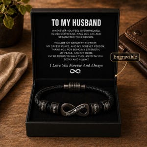 Op de afbeelding: Een zwarte gevlochten leren armband met metalen kralen met de namen James, Ethan, Daniel, Sophia, Mason en Liam, plus een oneindigheidssymbool. Gepresenteerd in een zwarte doos met de tekst TO MY HUSBAND en een hartverwarmende boodschap.