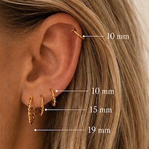 May include: Four gold hoop earrings with a twisted texture worn in the ear. The hoops are labeled with sizes 10 mm, 15 mm, and 19 mm, indicating the diameter of each piece. The jewelry features a consistent metallic gold finish and design.