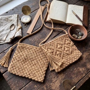 May include: Two beige macrame crossbody bags with long braided straps and decorative tassels. One bag features a simple knotted grid pattern, while the other displays a complex diamond-shaped knot design. Both bags are square-shaped and neutral.
