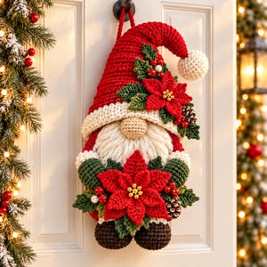 May include: A crocheted Christmas gnome wall hanging featuring a tall red hat with a white pom-pom, a thick white yarn beard, and dark brown feet. The gnome is decorated with red poinsettia flowers, green leaves, small red berries, and pinecones.