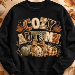 Könnte beinhalten: Ein schwarzes Langarm-Sweatshirt mit dem Schriftzug COZY AUTUMN in einer Patchwork-Schriftart mit verschiedenen Mustern. Unter dem Text befinden sich drei Kürbisse aus unterschiedlichen Stoffen, darunter ein mittlerer mit einer großen beigen Schleife.
