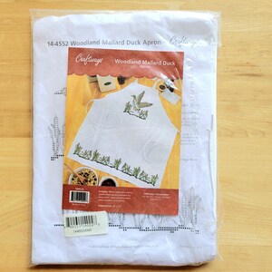 May include: A white apron kit with a printed design of a mallard duck and reeds. The kit is packaged in a clear plastic bag and includes the text "Woodland Mallard Duck Apron" and "Craftways". The apron design features a duck in flight.