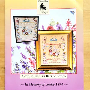 May include: A printed antique sampler reproduction featuring two framed cross-stitch samplers. The larger sampler, framed in gold, displays floral and butterfly motifs with the text "In Memory Of Louise Teegen 1874." The background is adorned with floral illustrations.