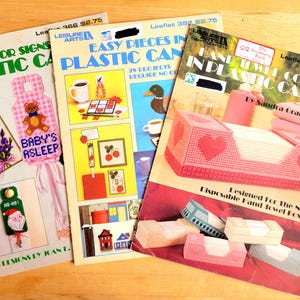 May include: Three plastic canvas craft patterns. The first pattern is for door signs, the second is for easy pieces in plastic canvas, and the third is for hand towels in plastic canvas. The patterns are all in color and feature various designs.