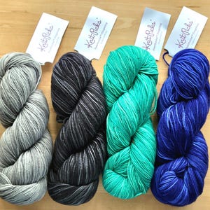 May include: Four skeins of Knit Picks Hawthorne Fingering yarn in light gray, dark charcoal, bright turquoise, and deep blue. Each skein features a tonal, variegated color pattern and includes a white paper tag with the brand name printed on it.
