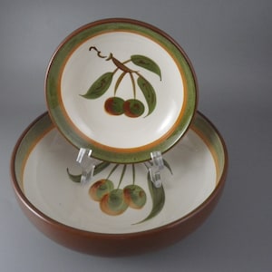 May include: Two-piece ceramic serving set featuring a large bowl and a smaller plate. Both pieces have a white interior with a painted cherry branch design in green, brown, and orange. The rims are trimmed in green and brown.