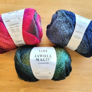 May include: Three skeins of Lang Jawoll Magic Superwash yarn in vibrant colors. One skein is a blend of pinks and reds, another is blue and gray, and the third is green and yellow. Each skein has a white label.