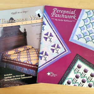 May include: Two quilting books are displayed on a wooden surface. One book, "Tennessee Waltz Quilt," features a bed and quilt design. The other, "Perennial Patchwork," has a magenta cover with quilt block illustrations.