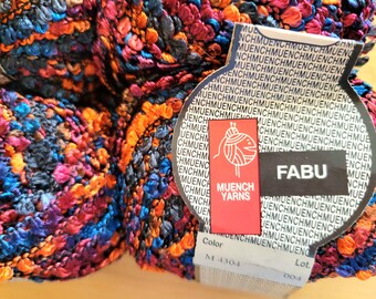 May include: Close-up of a colorful yarn ball with a textured, bumpy surface. The yarn features a mix of blue, orange, pink, and purple hues. A label reads "FABU" and "MUENCH YARNS".