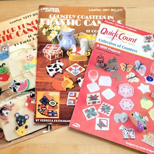 May include: Three vintage craft pattern booklets for plastic canvas projects. The booklets feature designs for coasters, lunch bags, and other decorative items. The covers display colorful finished projects, including animals and geometric patterns.