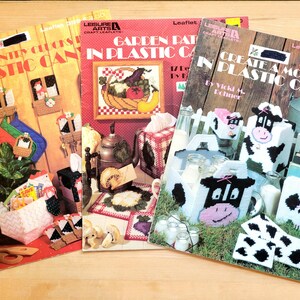 May include: Three plastic canvas craft leaflets with colorful images and instructions. The first leaflet is titled "Country Chic Plastic Canvas", the second is titled "Garden Path in Plastic Canvas", and the third is titled "Create a Moo-d in Plastic Canvas".