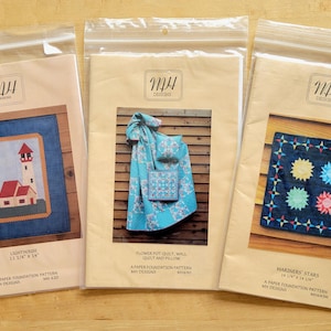 May include: Three packaged paper foundation patterns for quilting. The patterns are in clear plastic bags with kraft paper backing. The patterns include a lighthouse, a flower pot quilt, and a mariners' stars design. The lighthouse pattern measures 11 1/4" x 14".