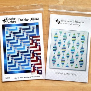 May include: Two quilting pattern packets in plastic sleeves. One packet is labeled "Twister Waves" with a blue and white design. The other packet is labeled "Sugar Sand Beach" with a diamond pattern in shades of blue and green.