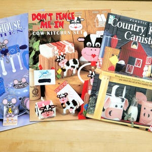 May include: A set of three ceramic mugs with a speckled, cream-colored glaze. Each mug features a different hand-painted floral design in shades of blue, green, and yellow. The mugs have a simple, rounded shape and a comfortable handle.