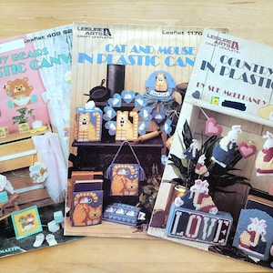 May include: Three Leisure Arts craft leaflets featuring plastic canvas projects. The left shows Baby Bears, the center displays Cat and Mouse, and the right features Country Bunnies. Each cover displays finished projects with colorful yarn designs.