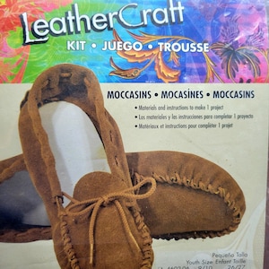 May include: A LeatherCraft kit for making brown suede moccasins. The packaging features the text LeatherCraft KIT JUEGO TROUSSE and MOCCASINS MOCASÍNES MOCCASINS. It includes materials and instructions for one project, with a youth size 11/12 selected.