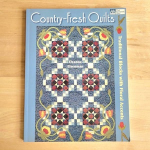May include: A book titled "Country-Fresh Quilts" with the subtitle "Traditional Blocks with Floral Accents" by Deanne Eisenman. The cover features a blue background with a quilt design in red, white, and black squares, and floral accents.