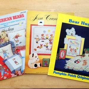 May include: Three softcover cross-stitch pattern booklets titled All-American Bears, Jessa Country, and Bear Hugs. Each booklet cover features colorful illustrations of teddy bears, instructional text, and finished project examples for embroidery.