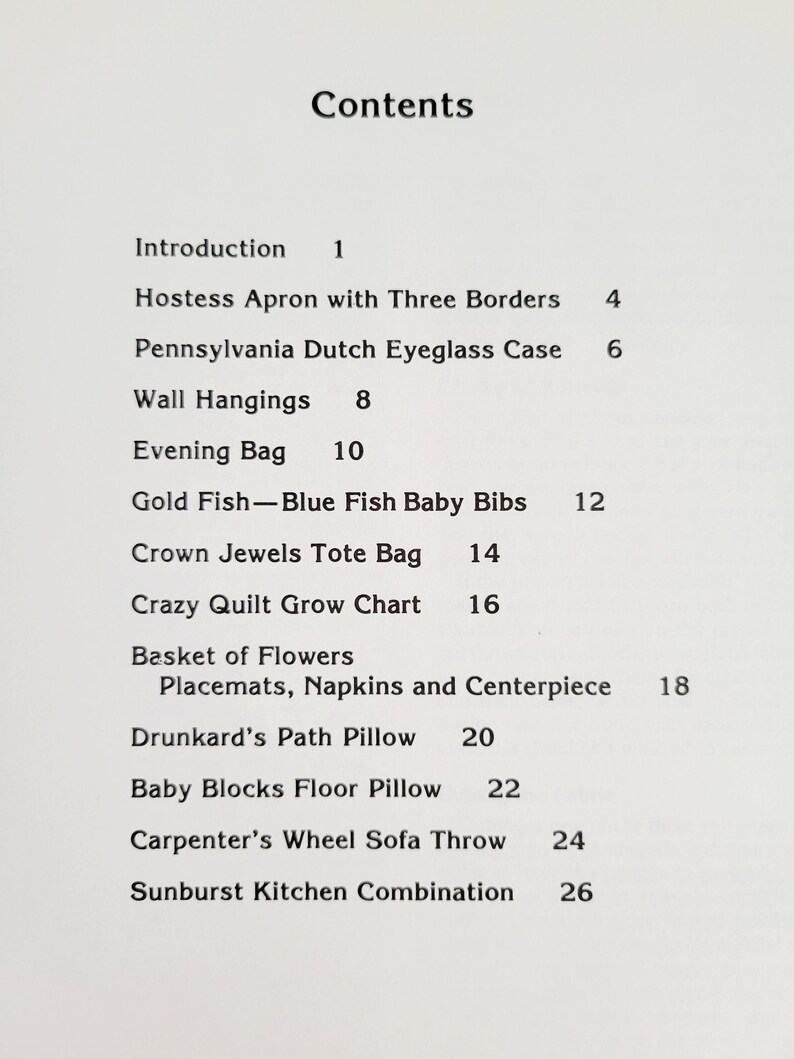 May include: A printed page with the title "Contents" at the top. The page lists various craft projects, including an apron, eyeglass case, wall hangings, an evening bag, baby bibs, a tote bag, and a grow chart.
