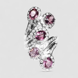 May include: A silver-toned ring featuring four oval-cut pink gemstones arranged in a cluster. Each gemstone is surrounded by a halo of small, clear, round-cut stones. The band is split and also encrusted with small, clear, round-cut stones.