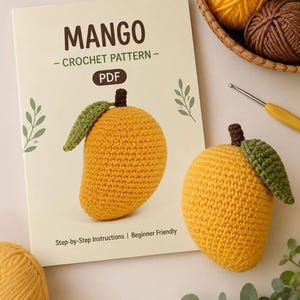 May include: A rectangular document titled MANGO - CROCHET PATTERN - PDF featuring a yellow crocheted mango with a green leaf and brown stem. Beside it sits a finished yellow crocheted mango, a yellow crochet hook, and balls of yarn.