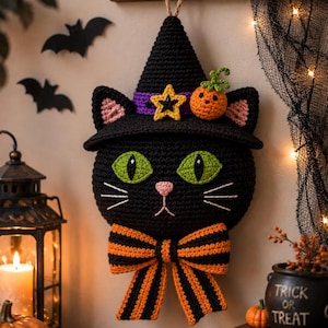 Può includere: Una decorazione da parete a forma di gatto nero all'uncinetto che indossa un cappello da strega nero con una fascia viola, una stella gialla e una piccola zucca arancione. Il gatto ha occhi verde brillante, naso rosa, baffi bianchi e un grande papillon a righe arancioni e nere.