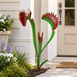 May include: A metal garden sculpture featuring three Venus flytrap plants with vibrant green stems and leaves. Each plant has a wide, open trap with deep red interiors and jagged, tooth-like edges, creating a striking botanical display.