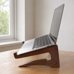 May include: A dark brown wooden laptop stand with a curved, ergonomic profile supporting a silver laptop at an angled position. The stand features a smooth, polished finish and a notched front edge to securely hold the device in place while in use.
