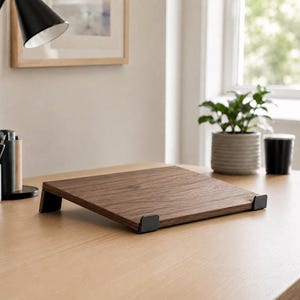 Peut inclure: Un support pour ordinateur portable en bois brun foncé avec une surface plate inclinée et un grain de bois naturel. Le support comporte deux supports métalliques noirs sur le bord avant pour maintenir l'appareil et deux pieds métalliques noirs.