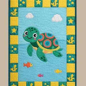 May include: A rectangular quilt featuring a central light blue panel with a green sea turtle, two white clouds, and three small orange and pink fish. The border consists of alternating yellow and green squares with yellow star and coral motifs.