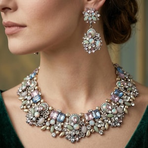 Könnte beinhalten: Ein Statement-Halsband und passende Ohrhänger mit einer Ansammlung von irisierenden, opalartigen Cabochons, hellblauen rechteckigen Kristallen und klaren facettierten Strasssteinen auf einer dunklen Metallbasis, die ein dichtes Blumenmuster bilden.