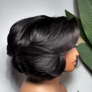 May include: A short, layered black wig with a voluminous, rounded silhouette and side-swept bangs. The hair features a smooth, straight texture with subtle inward-curving ends, styled to frame the face in a classic, chin-length bob cut.