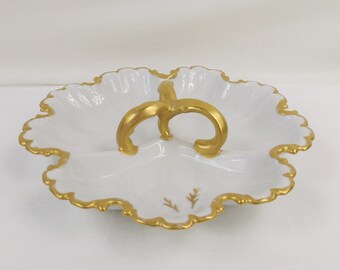 May include: A white porcelain serving dish with three sections and a gold handle. The dish has a scalloped edge and is decorated with a gold trim and a small floral design.