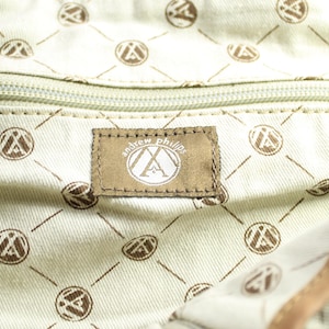 May include: Close-up of a bag's interior. The light beige lining features a repeating pattern of brown circles and diagonal lines. A brown label with "andrew phillips" is visible.