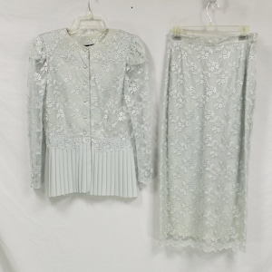 May include: A light blue lace jacket and skirt set. The jacket has a button-up front and a pleated hem. The skirt is a-line and has a lace trim.