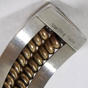 May include: A silver bracelet with a row of gold beads. The bracelet is marked "Sterling Tahe."