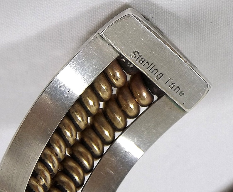 May include: A silver bracelet with a row of gold beads. The bracelet is marked "Sterling Tahe."