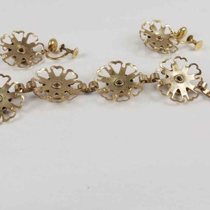 May include: A gold-tone bracelet and earrings set featuring a floral design. The bracelet has a chain with a clasp and the earrings are clip-on.