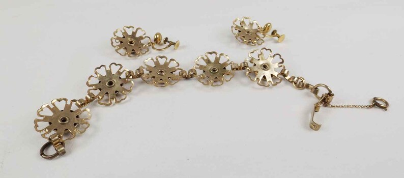 May include: A gold-tone bracelet and earrings set featuring a floral design. The bracelet has a chain with a clasp and the earrings are clip-on.