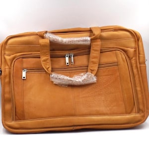 May include: A large, tan leather briefcase with multiple compartments and a top handle. The bag features silver-toned zips and hardware. The leather has a slightly distressed appearance, suggesting a vintage or rustic style. The briefcase is designed for carrying documents and other essentials.